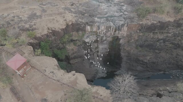 Raw footage, A cinematic drone view capturing birds are flaying and a dry waterfall hidden deep within a forest landscape.