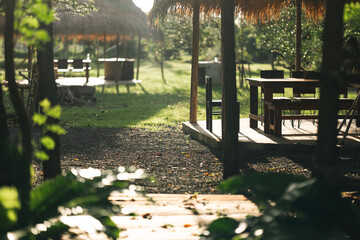 Naklejka premium Outdoor cafe garden table wooden chair sunlight summer green nature grass relax leisure countryside outdoor cafe with wooden table and chair straw roof warm sunlight, peaceful garden setting with