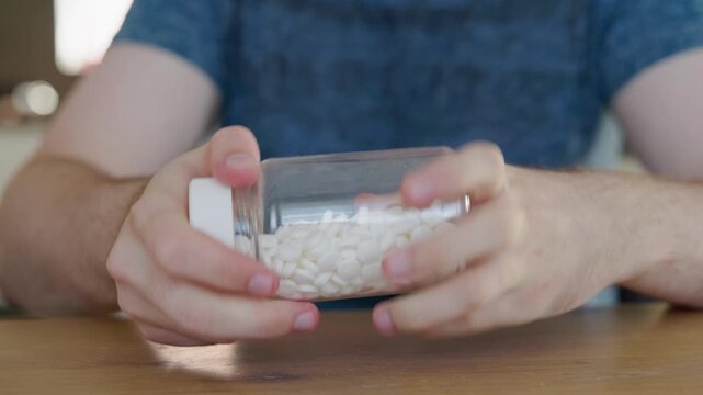 Man unsuccessfully trying to open child resistant medicine bottle with tablets, frustrated while struggling with safety cap