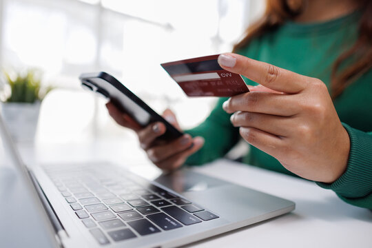 This image portrays a person holding a mobile phone and a credit card, focused on typing on a laptop, illustrating the seamless blend of technology in daily routines.