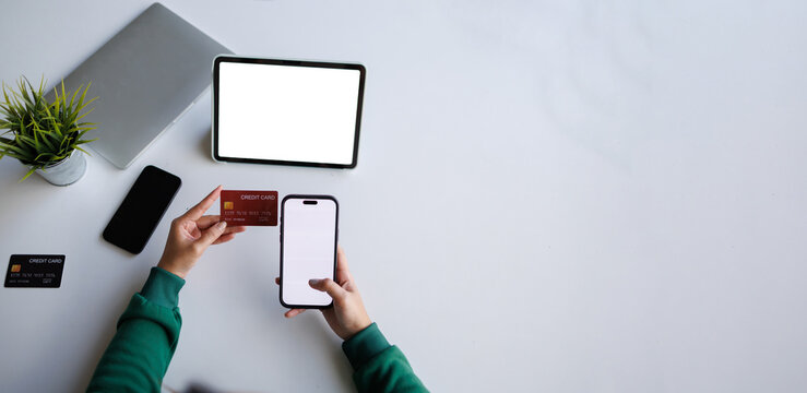 A person is holding a credit card while using a mobile device, depicting an online transaction process in a modern setting with a laptop nearby.