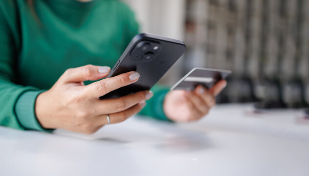 A person is engaged in a financial transaction with a smartphone in one hand and a credit card in the other, showcasing modern online shopping habits and technology.