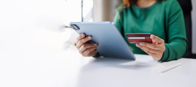 An individual is securely holding a tablet along with a red credit card, ready to make a purchase, representing the modern consumer's experience in digital commerce.