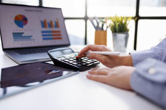 A pair of hands with a tablet and calculator, engaged in financial analysis while surrounded by graphical data in a contemporary office setting, emphasizing modern work dynamics.