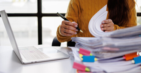 An individual engages in document review amidst stacks of papers, portraying real office dynamics...