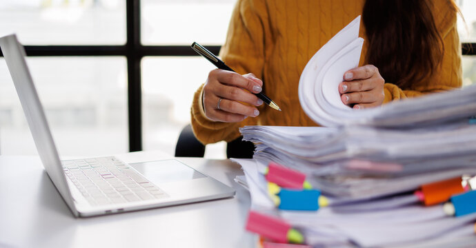 An individual engages in document review amidst stacks of papers, portraying real office dynamics and the complexities of managing numerous files and paperwork.