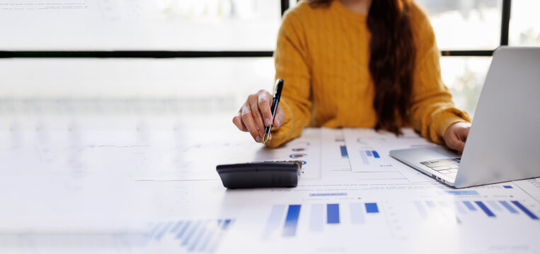 A dedicated individual is interacting with a calculator while analyzing reports and figures, illustrating the intensive nature of modern office tasks and data-driven decision-making.
