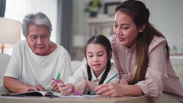 Grandmother and mother sit closely with a young girl, guiding her as she colors in a book with bright pencils, sharing a warm three-generation learning moment at home.