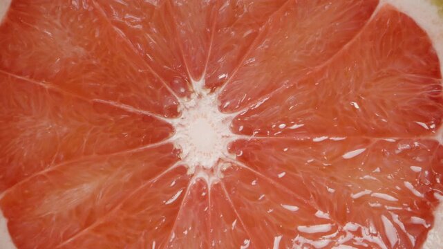 Macro zoom, a half of a grapefruit with red juicy flesh on a wooden table. Dolly slider.