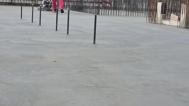 Low angle distant shot of a worker using a power trowel machine to smooth fresh concrete on a foundation slab.