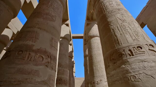 Karnak Temple in Luxor, Egypt. Looking up at colossal papyrus columns covered in hieroglyphics and red pigment inside Karnak Temple, Luxor Egypt.