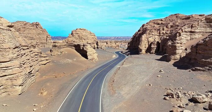 Aerial view of a winding asphalt road through Yardang rock formations in the Xinjiang desert, China. Drone perspective.