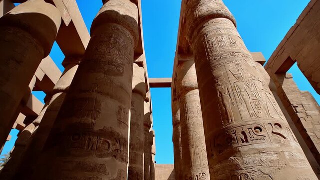 Dramatic low-angle view of enormous carved columns in Karnak Temple Hypostyle Hall, Luxor Egypt. Ancient red painted hieroglyphics on towering sandstone pillars.