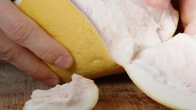 Close-up of male hands peeling pomelo from its thick peel.