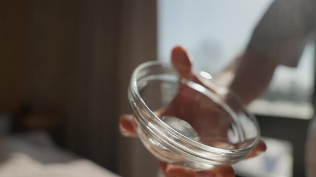 Close-up of a therapist gently pouring warm massage oil from a glass bowl onto a woman bare back in a serene spa room with soft natural daylight