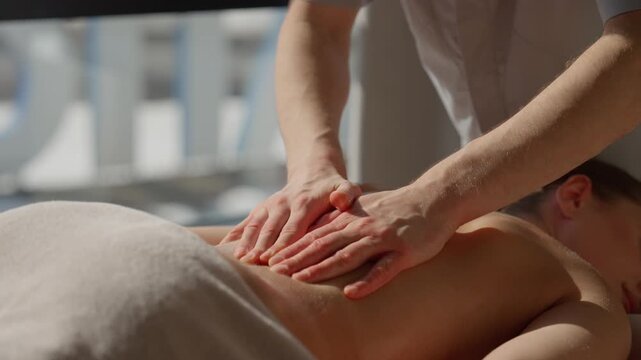Relaxing full body massage therapy with professional masseur hands gently massaging woman back and shoulders in tranquil spa wellness setting with soft natural light