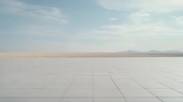 Expansive salt flat desert showing a vast, tiled surface extending into the horizon, with distant mountains under a clear blue sky, evoking concepts of space and openness