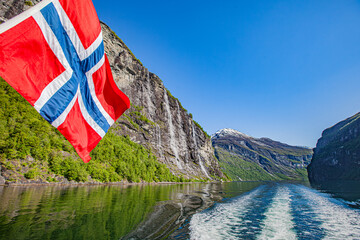 Bandera Noruega ondeando con la cascada de las siete hermanas de fondo navegando por el fiordo Geiranger. © Elkspera