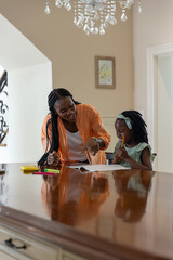 African American mother and daughter sitting at wooden table, mother in orange pointing at book