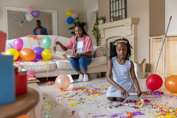 African American family tidying living room, child sweeping confetti, brush and dustpan, copy space
