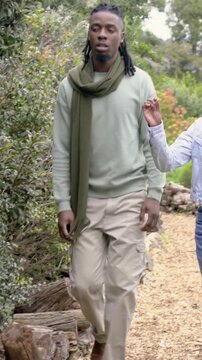 Vertical video: Noticing plants, walking couple gesturing at shrubs on wood-chip path, denim jacket