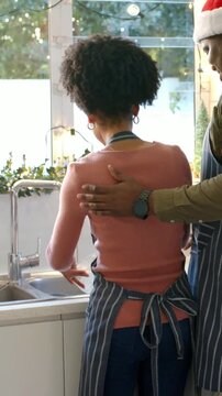Vertical video: Washing woman in pink top rinsing plates at sink, man in apron placing hand helping