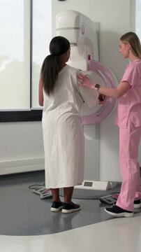 Vertical video: Exam starting gowned patient entering mammogram, tech aligning chest to pink paddle