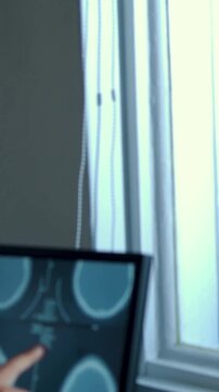 Vertical video: Leaning woman in short sleeve with watch tapping CT monitor at desk assessing scans