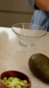 Vertical video: Starting meal prep, denim-clad cook slicing red pepper on cutting board with knife