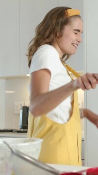Vertical video: Picking wooden spoon, woman in pinafore miming at counter with bowl, friend copying