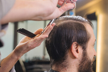 Barber cutting male client hair with scissors and comb. Close up of professional haircut process, precision technique, men grooming service in modern barbershop.