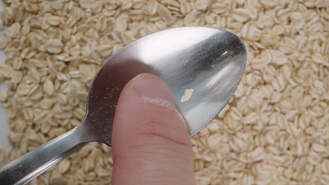 I shake off oat flakes from the spoon with my finger. Close-up against the background of oats.