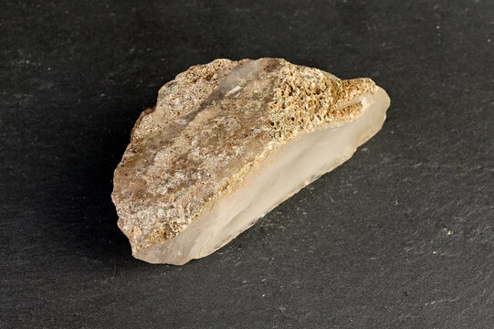 Close-up of a rough, translucent quartz crystal fragment on a dark slate background