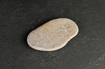 Obraz premium Smooth, rounded pebble resting on a dark, textured stone surface