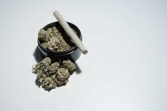 Marijuana joint on top of a black grinder with buds isolated on white