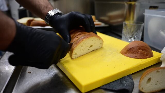 Chef in black gloves slicing bread on a yellow cutting board