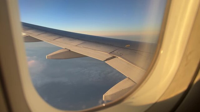 Passenger&rsquo;s view from airplane window, wing visible against a stunning sunset sky&mdash;vivid colors and peaceful atmosphere above the clouds.