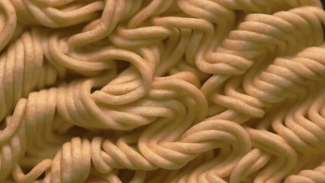 Top view of raw instant noodles block rotating. Macro texture of dry yellow ramen spinning. Close up food product details, wavy pasta pattern, fast food concept, overhead shot