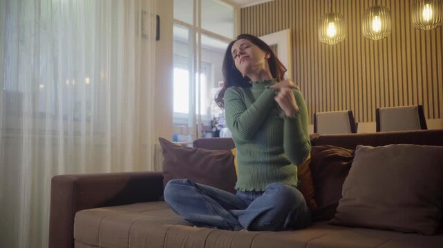 video of tired young caucasian woman painful with neck pain body ache from work, holding massaging rubbing shoulder hurt, sore sitting alone on sofa at home. Pain body muscles stiff problem