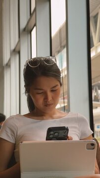 Asian woman using mobile phone while working with computer in the cafe.