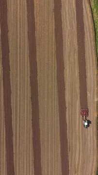 Tractor Cultivating Agricultural Field: An aerial perspective of a tractor methodically tilling neat, parallel rows across a vast, golden agricultural field.