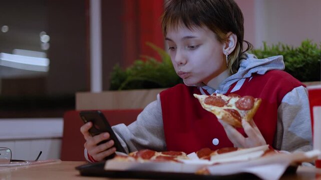 Social media takes over as a teenage girl sits in a fast food restaurant, phone glued to her hand, enjoying her pizza slice without ever looking up from the screen. Real time video.
