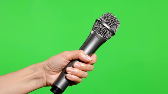Hand holding professional microphone against green screen background for interview podcast or karaoke singing concept and media production