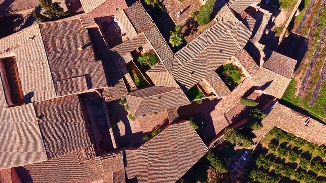 Aerial view showcases a cluster of buildings with tiled roofs surrounded by plants and pathways, set in a vineyard area under clear skies during daylight