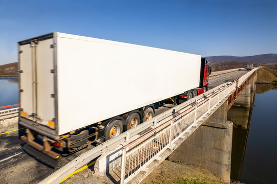 Red truck with white trailer moving on a bridge over the river