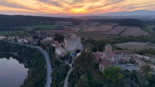 Cinematic drone flight over Penedes wine region at golden hour. Sunset view of Castellet castle, traditional Spanish village, and Foix reservoir lake.