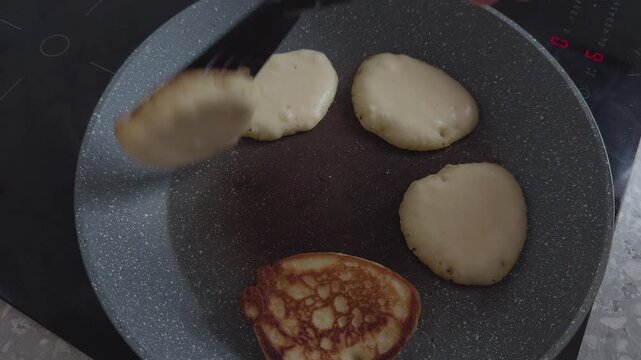 A close-up of golden brown gluten-free pancakes flipping with a spatula in a grey frying pan.