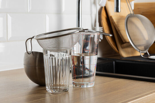 A clear kitchen scene with a strainer and glasses on a countertop.