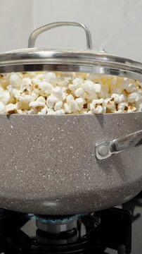 Vertical video. The pot of popcorn on the gas stove, the lid lifts due to the excess kernels, causing them to spill over the edge.