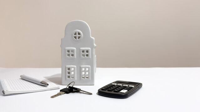 White ceramic house model on a desk with keys, calculator, and notebook for real estate, mortgage, and home insurance planning with copy space
